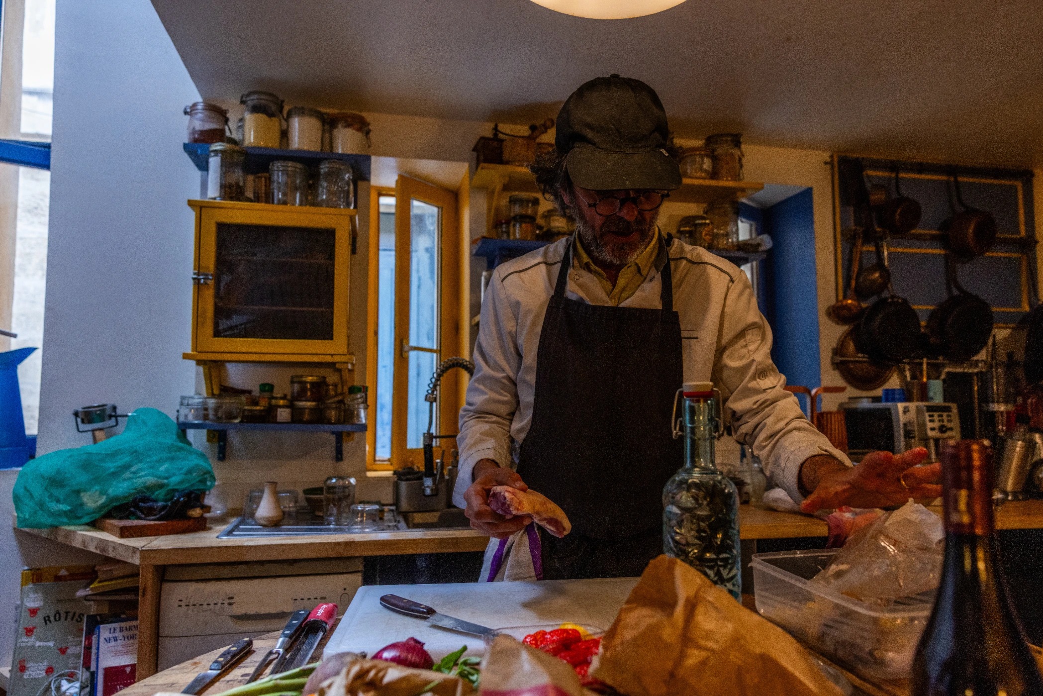 Le chef Éric Deup prépare le repas dans la cuisine du chalet, entouré de bocaux et de cuivres